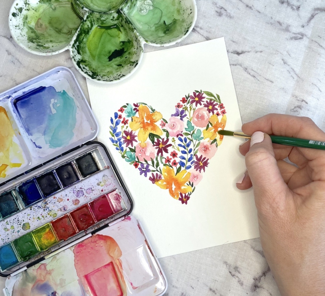Hand using paint to make a multicolored floral heart using waterpainting technique
